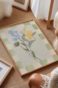 a woman sitting on the floor next to a painting with flowers painted on it in front of her