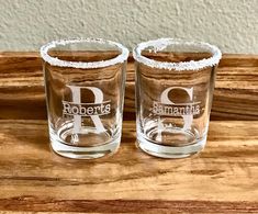 two shot glasses sitting on top of a wooden table with the letters d and p