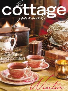 the cottage journal cover features tea cups and saucers on a table in front of a fireplace