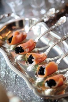 small appetizers are arranged on a platter with silver spoons and blackberries