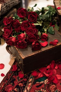 a bunch of red roses sitting on top of a piece of brown luggage with petals scattered around it