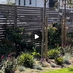 a garden with lots of plants and flowers in the grass next to a wooden fence