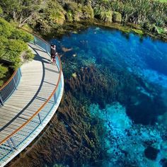 people are standing on a bridge over the water and looking at the blue hole in australia