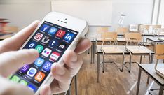 a person holding an iphone in front of a classroom full of desks and chairs