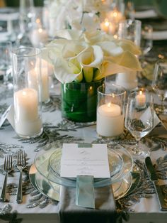 the table is set with silverware, candles and white flowers in a green vase