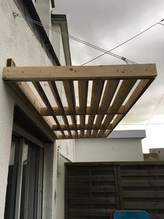 a wooden pergolan attached to the side of a building with a blue chair under it