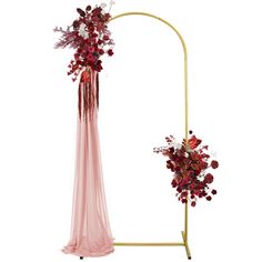 a pink and red flower arrangement on a gold stand with a white backdrop in the background