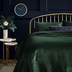 a bed with green bedspread and pillows in front of a black wall next to a side table