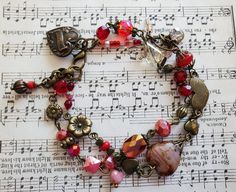 a close up of a bracelet on top of sheet music with red beads and charms