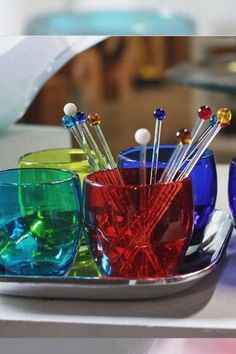 colorful glass cups and spoons sitting on a plate with toothbrushes in them