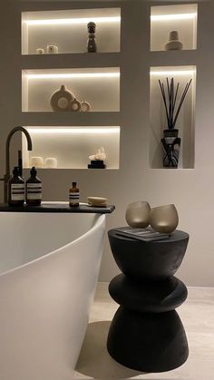 a white bath tub sitting next to a sink under floating shelves filled with vases