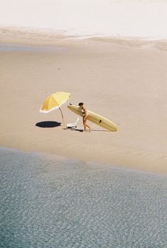 a person with a surfboard and an umbrella on the sand at the water's edge