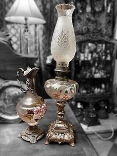 two antique glass vases sitting on top of a wooden table next to a lamp