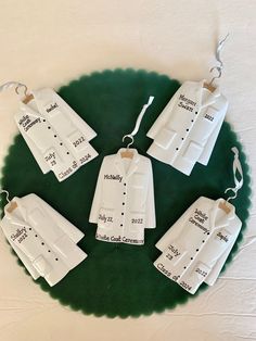 five ceramic clothes hang on a green platter with name tags attached to the shirts