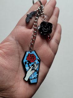 a hand holding a key chain with a rose on it and two black keys attached to it