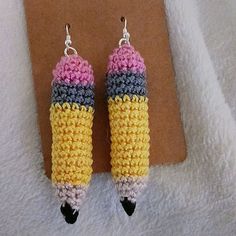 two crocheted earrings hanging from hooks on a piece of paper next to a pair of scissors