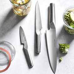 there are three knives on the table next to some broccoli and lemons