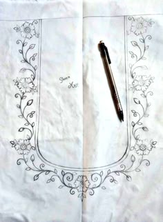 a pen sitting on top of a piece of paper next to an embroidered frame with flowers and vines