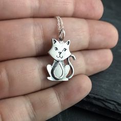 a hand holding a silver cat charm on a chain