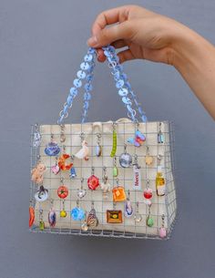 a hand is holding a purse with many charms on it and hanging from the handle