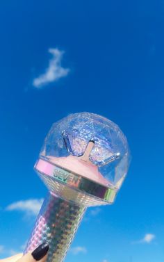 a hand holding a plastic object in the air with blue sky and clouds behind it