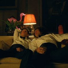 two men in tuxedos are laying on a couch with a lamp next to them