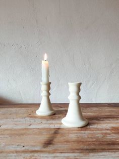 two white candlesticks sitting on top of a wooden table next to each other