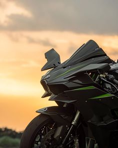 the motorcycle is parked on the side of the road near the grass and trees as the sun sets