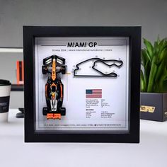 a framed photograph of a race car on display next to a coffee cup and plant