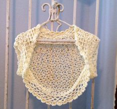 a white crocheted shirt hanging on a metal rack in front of a blue wall