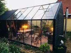 a small black building with some lights on it's windows and chairs outside in the grass