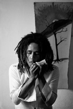 a man with dreadlocks eating something in front of a painting on the wall