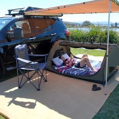 a person laying in a tent next to a car with the door open and an awning over it