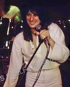 a smiling woman holding a microphone in front of her face and singing into the microphone