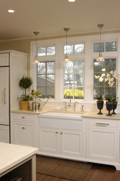 a kitchen with white cabinets and marble counter tops, two potted plants on the window sill