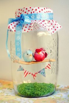 two birds sitting on a branch in a glass jar with blue ribbon and red apples