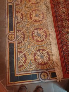 someone's feet are standing on the floor next to a rug with an intricate design