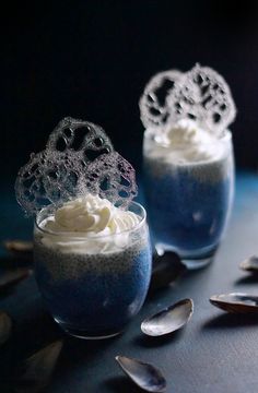 two glasses filled with blue pudding on top of a table next to silver spoons