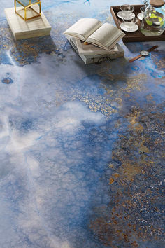 a room with blue and yellow paint on the floor next to a book, coffee table and lamp