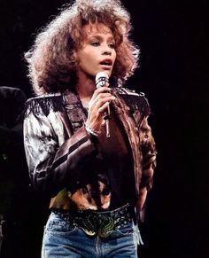 a woman holding a microphone in her right hand and wearing jeans on the other side