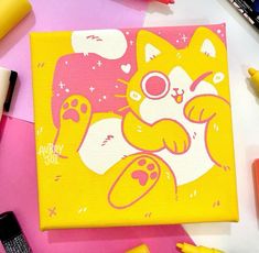 a yellow and white cat painting on a pink surface with markers, pens, and other items