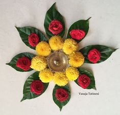 a flower arrangement with yellow and red flowers on a white table top next to green leaves