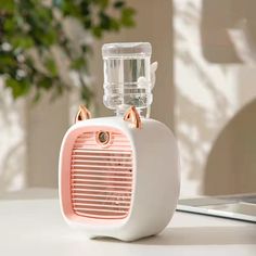 a white and pink speaker sitting on top of a table next to a laptop computer