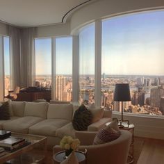 a living room filled with furniture and large windows overlooking a cityscape in the distance