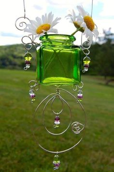 a green glass vase with daisies hanging from it's side in a field