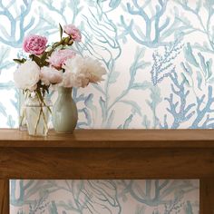 a vase with flowers on a table in front of a wallpapered background that looks like corals