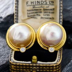 This show-stopping pair of earrings each feature a 17mm mabé pearl surrounded by a two-tiered gold frame. The bottom of the earring is accented with a round brilliant cut diamond in a full bezel setting. The earrings measure 24.0mm long by 23.3mm wide and 17.9mm deep.  They are finished with posts and omega backs. Formal Round Pearl Earrings With Polished Finish, Round Pearl Earrings With Polished Finish For Anniversary, Anniversary Pearl Earrings With Polished Finish, Yellow Gold Diamond Pearl Earrings With High Luster, Formal Gold Pearl Earrings Cabochon, Gold Cabochon Pearl Earrings, Luxury Yellow Gold Pearl Earrings With Brilliant Cut, Luxury Hallmarked Yellow Gold Pearl Earrings, Luxury Yellow Gold Round Pearl Earrings