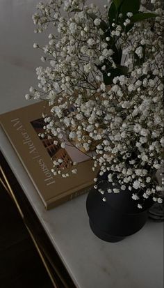 a vase filled with white flowers sitting on top of a table next to a book