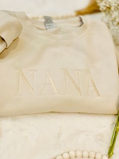 "This Monochromatic Customizable Embroidered NANA Crewneck Sweatshirt is the perfect gift for any mom or grandma for any occasion, Mother's day gift, Christmas gift, Birthdays gift This sweatshirt can be customized with a short word like (MAMA, DADA, MIMI, NANA, PAPA, WIFE, HUBBY, BRIDE, GROOM etc.) and up to 7 letters (GRANDMA, GRANDPA). Embroidery length will be anywhere between 6-9.5\" and height will be anywhere between 1.5-2.5\".  This embroidery color is a monochromatic look to match the color sweatshirt.  SWEATSHIRT DETAILS     High quality Midweight Pigment-Dyed Crewneck Sweatshirt - Independent Trading Co.    - 9 oz./yd² (US) 15 oz./L yd (CA), 80/20 ring-spun cotton/polyester blend with 100% cotton face, 30 singles     - Classic fit     - Color shown in Pigment Ivory Care Instruct Custom Embroidered White Tops For Mother's Day, Long Sleeve Tops With Letter Embroidery For Birthday, Embroidered Crew Neck Top For Birthday, Custom Embroidered Crew Neck Top For Birthday, Custom Embroidery Crew Neck Top For Birthday, Grandpa Embroidery, Gifts For Nana, Nana Birthday Gift, Nana Sweatshirt