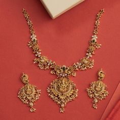 Description: This alluring necklace set from Tarinika features handcrafted designs decorated with temple elements surrounded with peacocks and flower motifs made of CZ stones and pearls on an antique gold base. Style this intricate temple set with any ethnic outfit. Details & Specifications:Materials used: Brass Alloy with Antique platingWeight - Necklace: 67 gms, Earrings: 29 gmsLength - Necklace: 19.5 cms, Earrings: 7.5 cmsMake it customWant to make it a custom necklace? Sure! Reach out to us Antique Simple Necklace, Antique Gold Set Designs, Intricate Gold Necklace, Kunden Necklace Set, Gold Necklace With Earrings Set, Gold Necklace Designs For Bride, Necleses Jewelry Gold Indian Latest, Tarinika Jewellery, New Model Necklace Designs Gold